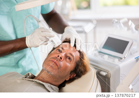 Man client undergoes facial skin care procedure using nozzle cold hammer whitening Man client undergoes facial skin care procedure using nozzle cold hammer whitening 137870217
