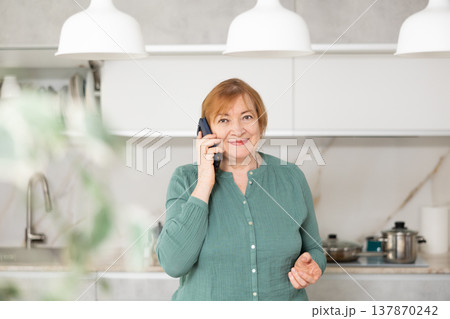 Positive mature woman is discussing something with someone on a mobile Positive mature woman is discussing something with someone on a mobile 137870242