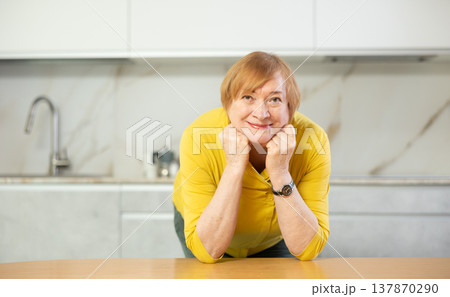 Happy older lady standing in kitchen with warm smile Happy older lady standing in kitchen with warm smile 137870290