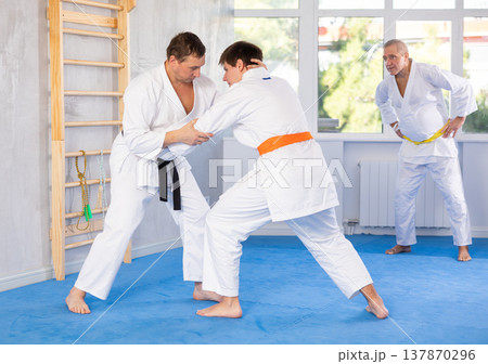 Experienced karate instructor demonstrating techniques in sparring with young fighter Experienced karate instructor demonstrating techniques in sparring with young fighter 137870296