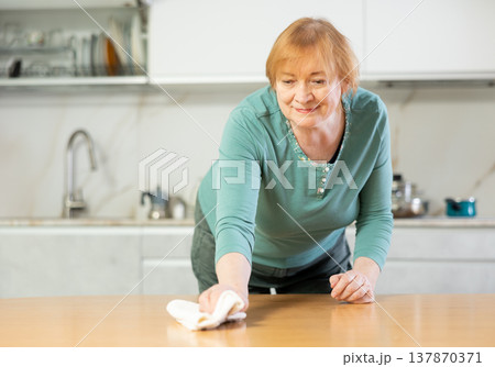Adult woman in casual clothes wipes table in kitchen 137870371