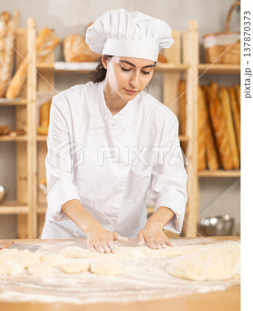 Young woman works as baker, mold baguette from dough, creates long loafs from dough. 137870373