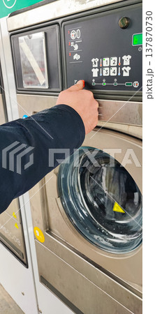 A man presses a button on the control panel of a washing machine at a self-service laundromat. Concepts of everyday life, automation, household services, and the use of modern household appliances A man presses a button on the control panel of a washing machine at a self-service laundromat. Concepts of everyday life, automation, household services, and the use of modern household appliances 137870730