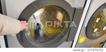 A man presses a button on the control panel of a washing machine at a self-service laundromat. Concepts of everyday life, automation, household services, and the use of modern household appliances 137870732