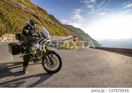 Motorcycle rider posing in Italian Alps during sunrise, dramatic sky. Travel and freedom, outdoor activities Motorcycle rider posing in Italian Alps during sunrise, dramatic sky. Travel and freedom, outdoor activities 137870838