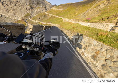Motorcycle rider riding in Italian Alps during sunrise , handlebar view , dramatic sky . Travel and freedom, outdoor activities Motorcycle rider riding in Italian Alps during sunrise , handlebar view , dramatic sky . Travel and freedom, outdoor activities 137870839