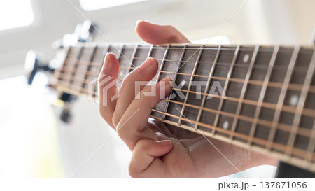 Close-up of a hand playing guitar strings, showcasing finger placement and wooden fretboard in a bright indoor setting with natural light 137871056