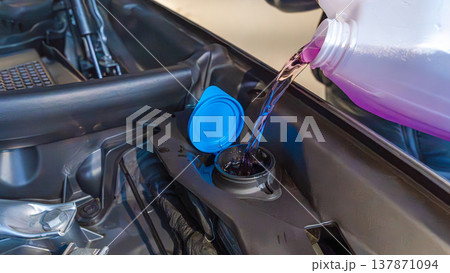 Pouring windshield washer fluid into a car reservoir with a blue cap, showcasing the engine compartment and surrounding components Pouring windshield washer fluid into a car reservoir with a blue cap, showcasing the engine compartment and surrounding components 137871094