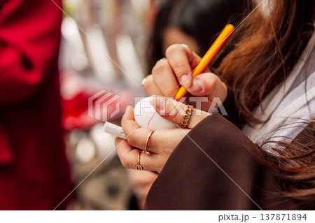 Hands Sketching Egg. Artist Sketching Vibrant Red Line On Egg Shell In Openair Workshop Setting Hands Sketching Egg. Artist Sketching Vibrant Red Line On Egg Shell In Openair Workshop Setting 137871894