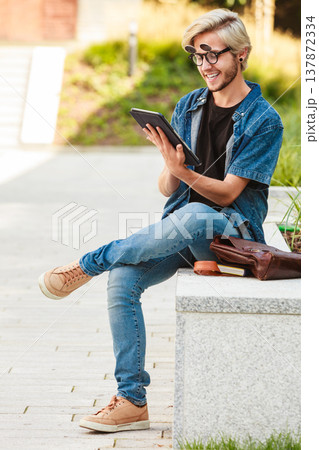 Hipster smiling guy with tablet sitting on ledge Hipster smiling guy with tablet sitting on ledge 137872334