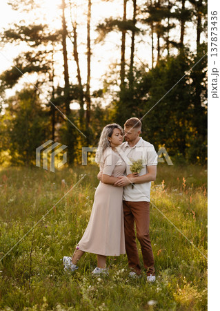 Young couple embracing in meadow at sunset with forest background 137873436