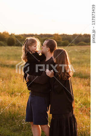 Family with little daughter standing in meadow at sunset Family with little daughter standing in meadow at sunset 137873439