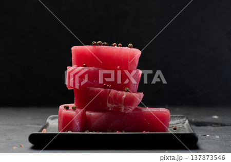 Stack of raw tuna pieces on black plate, black table 137873546