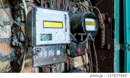 Old analog electricity meter stands next to a modern digital one in a dilapidated interior. Old analog electricity meter stands next to a modern digital one in a dilapidated interior. 137873884