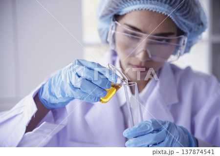 Scientist woman holding chemical test yellow glass tube testing science laboratory. Lab technician holding gold fluid drop to glass tube Urine sample. Asian woman scientist working medical chemistry Scientist woman holding chemical test yellow glass tube testing science laboratory. Lab technician holding gold fluid drop to glass tube Urine sample. Asian woman scientist working medical chemistry 137874541