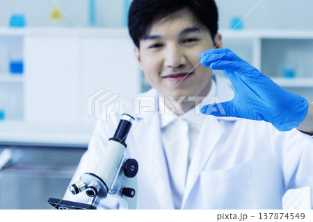 Scientist man look into Microscope research in science laboratory. Asian scientist look at microbiology microscope laboratory equipment chemistry lab. Biochemistry research experiment vaccine concept 137874549