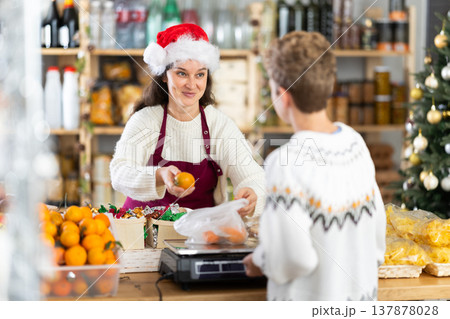 Woman sells fruits to teen boy, puts tangerines in bag, puts them on scale and weighs fruits 137878028