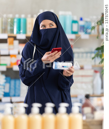 Woman in Muslim attire scanning QR code on box of ointment in pharmacy Woman in Muslim attire scanning QR code on box of ointment in pharmacy 137878045