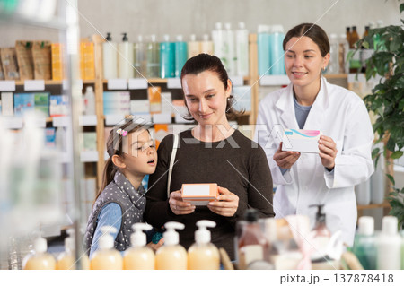Woman with daughter choosing box of medicine with pharmacist assistance in pharmacy Woman with daughter choosing box of medicine with pharmacist assistance in pharmacy 137878418