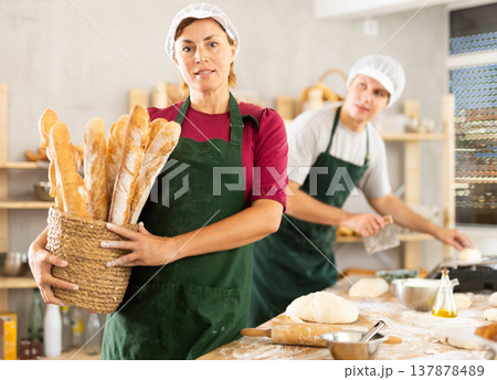 Adult woman baker with basket of baguettes Adult woman baker with basket of baguettes 137878489