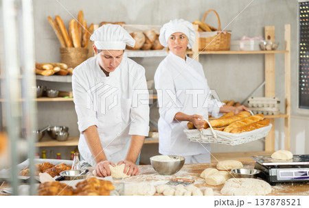 Male and female bakers knead dough and put baked goods Male and female bakers knead dough and put baked goods 137878521