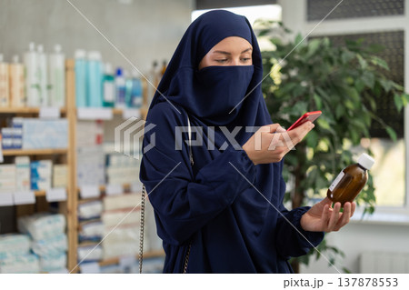 Young woman in niqab checking syrup medicine details on smartphone Young woman in niqab checking syrup medicine details on smartphone 137878553