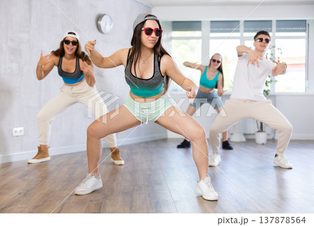 Group of young girls in dark glasses and ball cap and guy dance jazz-funk in fitness club. Group of young girls in dark glasses and ball cap and guy dance jazz-funk in fitness club. 137878564