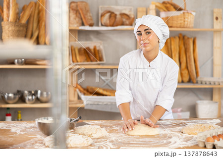 Young woman baker kneads the dough in bakery 137878643