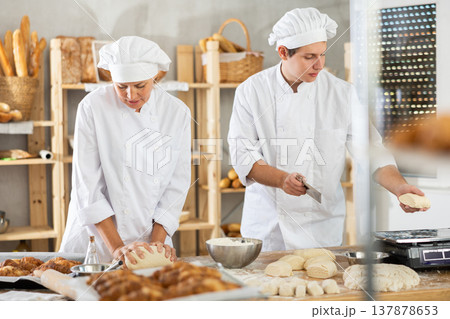 Male and female bakers knead dough, cut and weigh pieces Male and female bakers knead dough, cut and weigh pieces 137878653