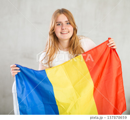 smiling girl in arms raised above head holds canvas of national flag of Romania 137878659