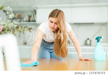 in kitchen,positive housewife in casual clothes holds rag in hands and cleans surface of table 137878733