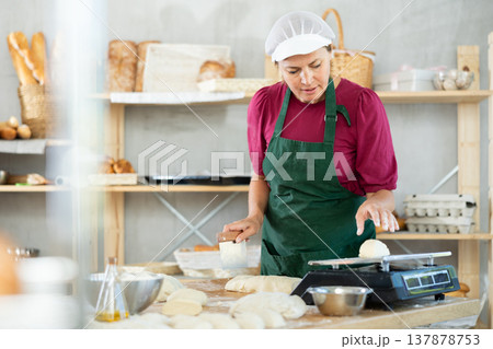 Woman baker cuts and weighs pieces of dough Woman baker cuts and weighs pieces of dough 137878753