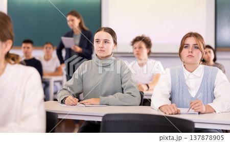 Girl and boy sitting at lesson in classroom, teacher standing Girl and boy sitting at lesson in classroom, teacher standing 137878905