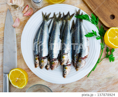 Fresh sardines lying on plate with lemon, parsley and garlic Fresh sardines lying on plate with lemon, parsley and garlic 137878924