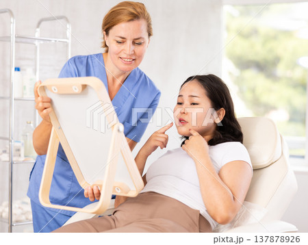 Middle-aged woman consulting with mirror Middle-aged woman consulting with mirror 137878926