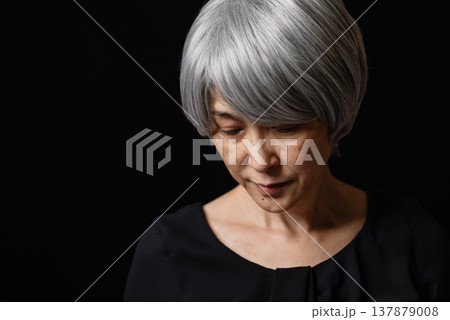 黒背景の前にいる俯く白髪のシニア女性 黒背景の前にいる俯く白髪のシニア女性 137879008
