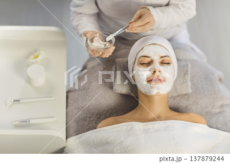 Female cosmetologist applying moisturizing mask to a young woman in spa salon. Female cosmetologist applying moisturizing mask to a young woman in spa salon. 137879244