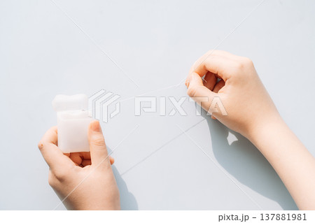 Child hands holding dental floss container and pulling floss on light blue background, oral hygiene concept Child hands holding dental floss container and pulling floss on light blue background, oral hygiene concept 137881981