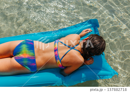 high angle view of one girl lying on pool float on a sunny day in the clear sea high angle view of one girl lying on pool float on a sunny day in the clear sea 137882718