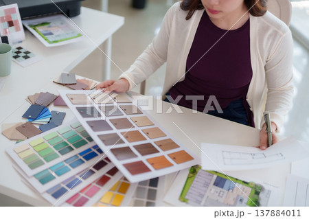 Asian adult woman designer selects color swatches material samples architectural blueprints plans home renovation creative diligent focused work modern office studio workspace 137884011