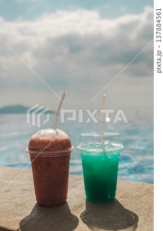 Two chilled drinks on pool edge with calm ocean horizon and soft sky creating tropical travel refreshment scene 137884561