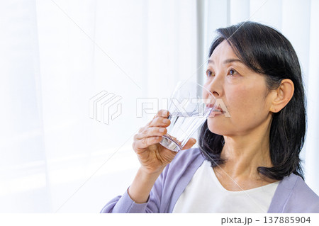 窓辺で水を飲むシニア女性 137885904