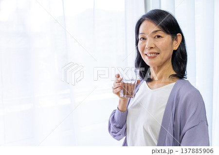 窓辺で水を飲むシニア女性 137885906