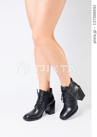 Fashionable woman in stylish leather shoes with heels. Female beautiful legs with fashionable boots in the studio on an isolated white background 137886692