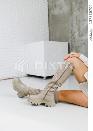Close-up of female legs in beige leather boots. Women's winter shoes. Warm women's boots Close-up of female legs in beige leather boots. Women's winter shoes. Warm women's boots 137886704