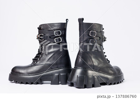 Women's shoes on a white background. Close-up of women's black leather boots with buckles on a white background. Shoes for the city. Concept for 2022 fashion, design and footwear. Women's shoes on a white background. Close-up of women's black leather boots with buckles on a white background. Shoes for the city. Concept for 2022 fashion, design and footwear. 137886760