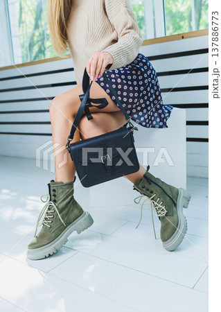 Fashionable leather boots on a woman's leg, close-up, fashionable. Leather bag in female hands. 137886773