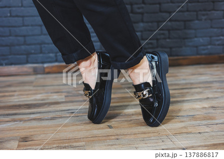 Close-up female legs in black trousers and leather black shoes. Women's shoes in patent leather with a metal buckle. New spring-summer collection of women's leather shoes 2022 137886817