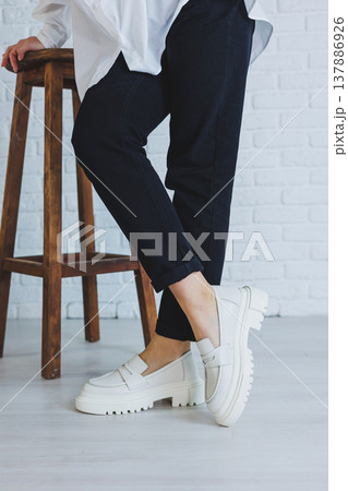 Legs of a young beautiful woman in black trousers and modern stylish white leather loafers. New collection of women's shoes spring-summer 2022 Legs of a young beautiful woman in black trousers and modern stylish white leather loafers. New collection of women's shoes spring-summer 2022 137886926