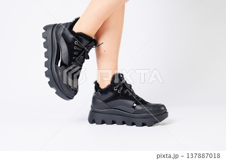 Fashionable black sneakers on the legs of a woman in the studio on a white background. Legs of a young girl with beautiful trendy shoes Fashionable black sneakers on the legs of a woman in the studio on a white background. Legs of a young girl with beautiful trendy shoes 137887018